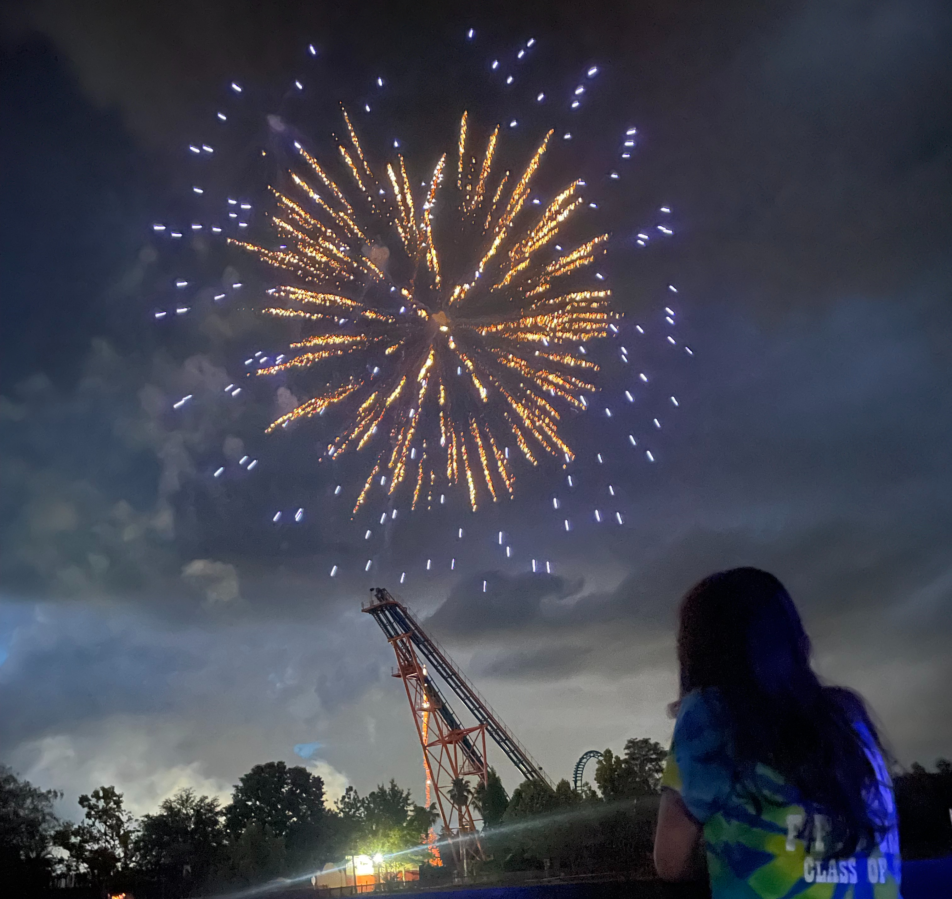 Girl watching firework explode over roller coaster