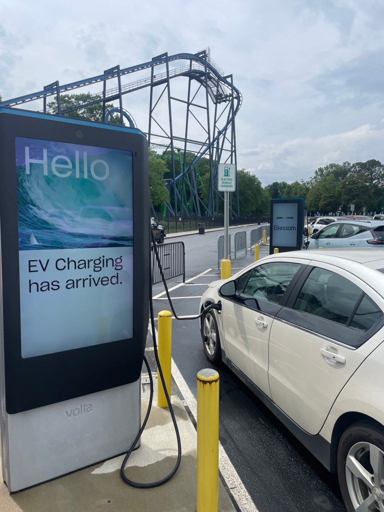 Car charging station at a theme park with roller coaster