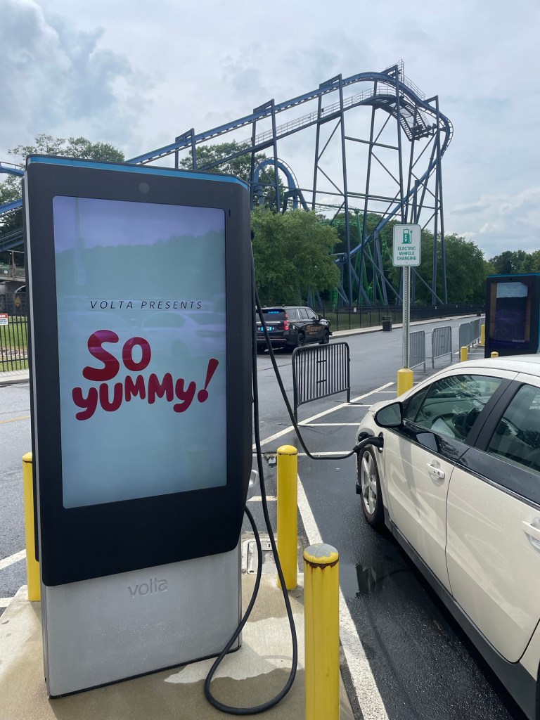 Car charging station at a theme park with roller coaster